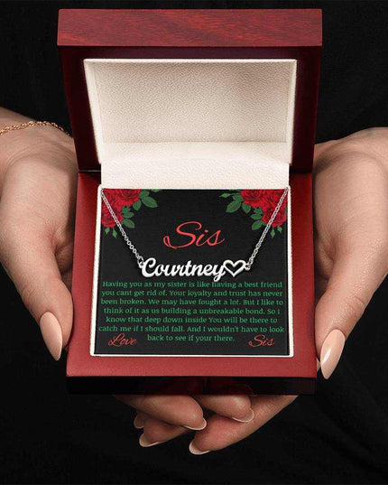 Name Heart Necklace with a polished stainless-steel variant on a To Sis from Sis greeting card inside a mahogany box up close view in the hands of a model.