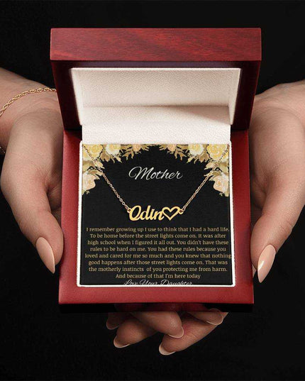 A yellow gold finish name heart necklace in a mahogany box being held.