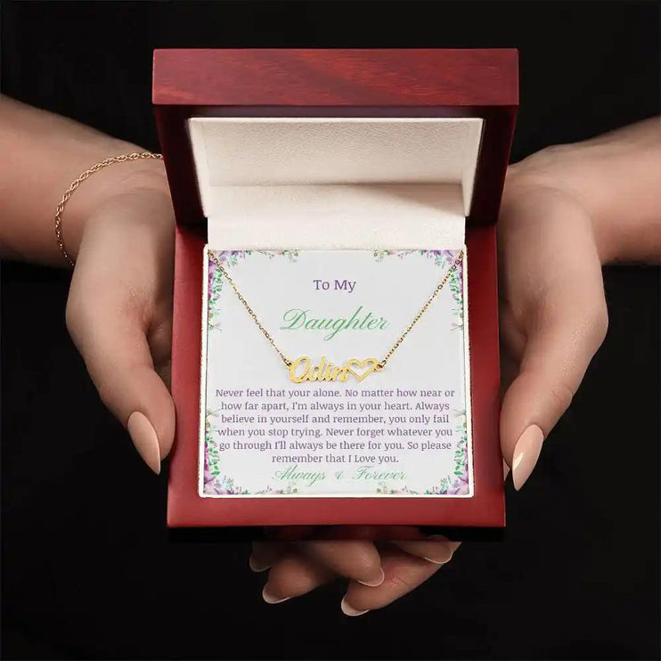 A yellow gold name heart necklace in a mahogany box in a models hands