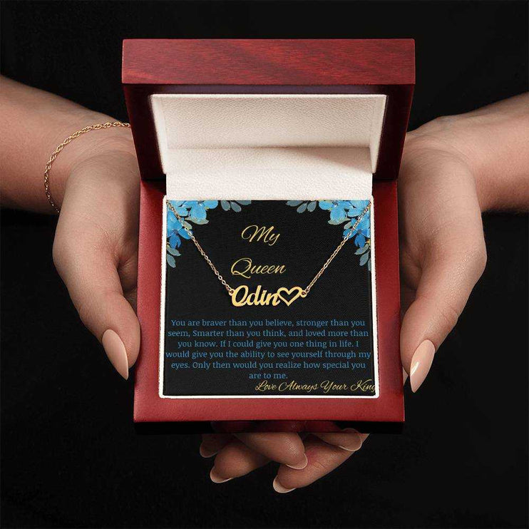 A yellow gold name heart necklace in a mahogany box with a to my queen greeting card in a models hands.