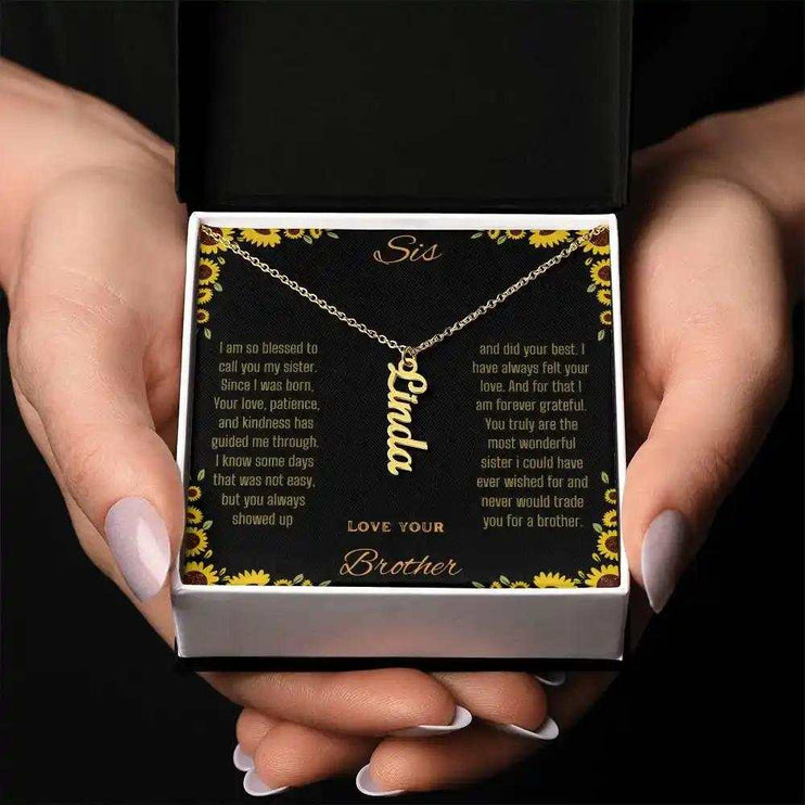 Vertical Name Necklace with a yellow gold finish charm on a to sis from brother greeting card inside of a two-tone box held in a models hands