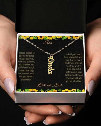 Vertical Name Necklace with a yellow gold finish on a To Sis From Sis greeting card inside a two-tone box close up in models hands