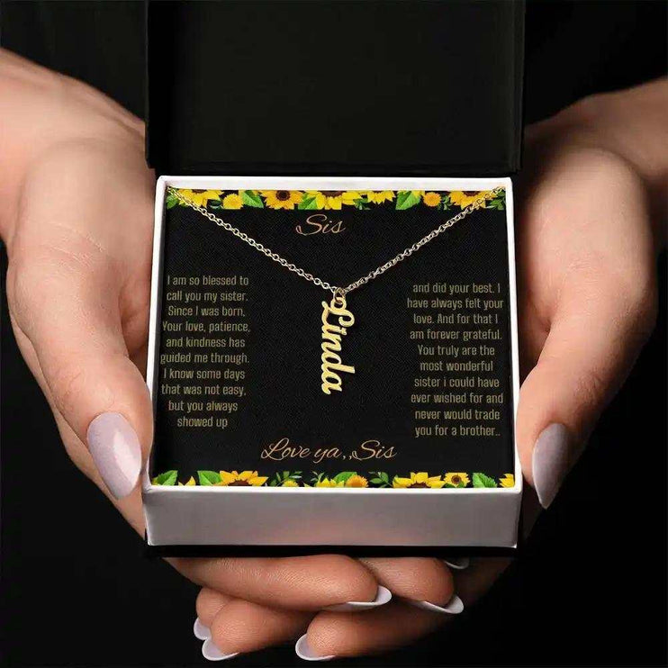Vertical Name Necklace with a yellow gold finish on a To Sis From Sis greeting card inside a two-tone box close up in models hands