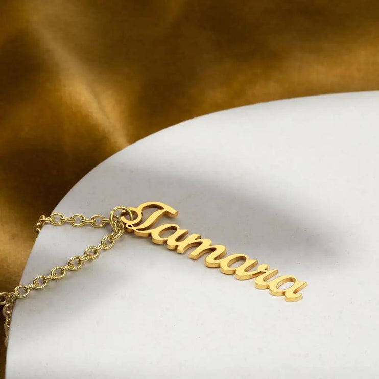 gold vertical name necklace on white table