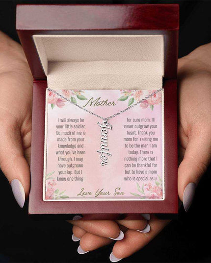 A polished stainless-steel vertical name necklace in a mahogany box in a models hands.