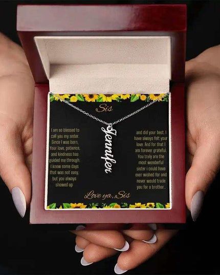 Vertical Name Necklace with a polished stainless-steel finish on a To Sis From Sis greeting card inside a mahogany box in a models hands
