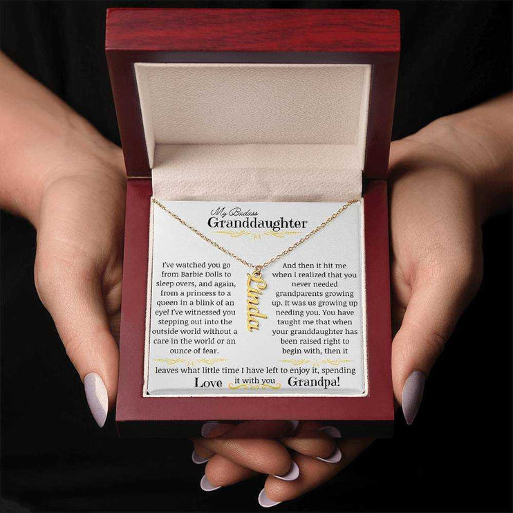 a yellow gold vertical name necklace up close in a mahogany box in a models hands.