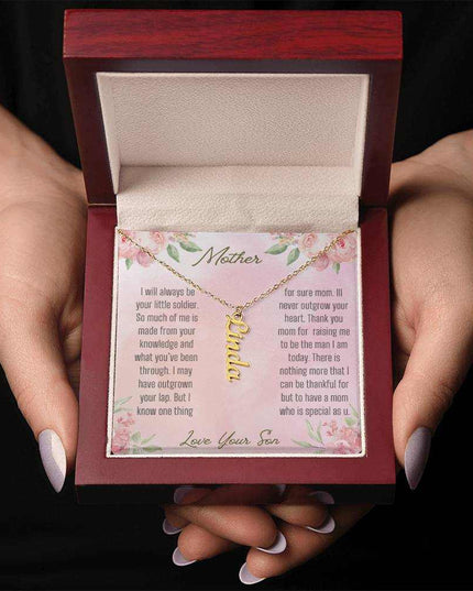 A yellow gold finish vertical name necklace in a mahogany box in a models hands.