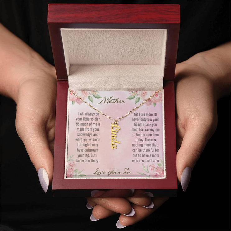 A yellow gold finish vertical name necklace in a mahogany box in a models hands.