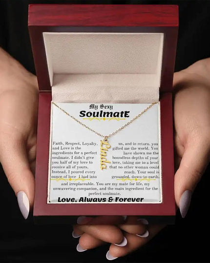 a yellow gold vertical name necklace in a mahogany box in models hands