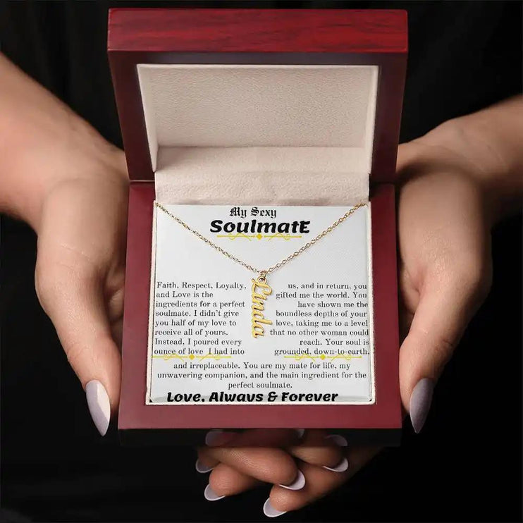 a yellow gold vertical name necklace in a mahogany box in models hands