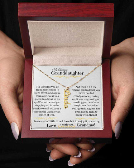 a yellow gold vertical name necklace in a mahogany box in a models hands