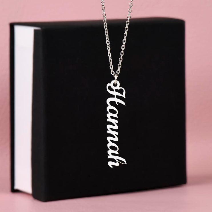 a polished stainless-steel vertical name necklace on top of a two-tone box