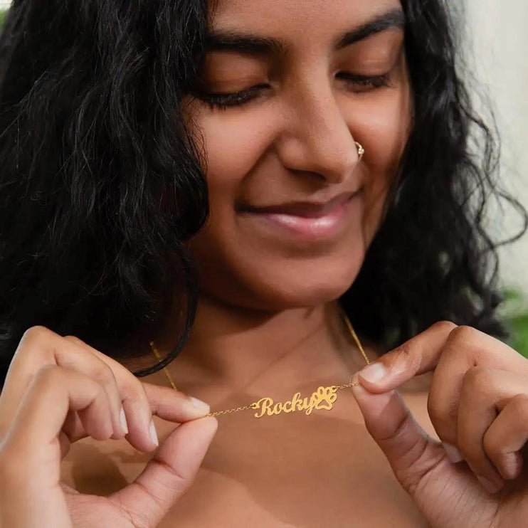 A yellow gold pet name paw print necklace on models neck