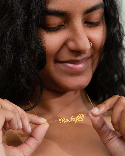 A yellow gold finish pet name paw print necklace on a models neck.
