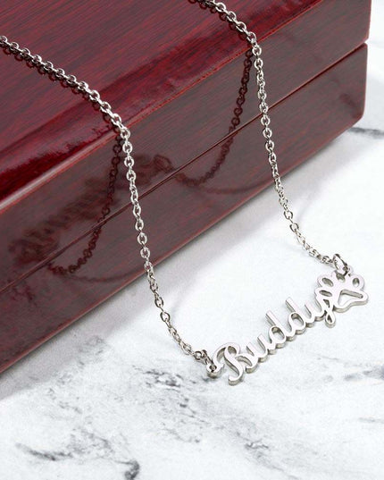 A polished stainless-steel pet name paw print necklace on top of mahogany box.