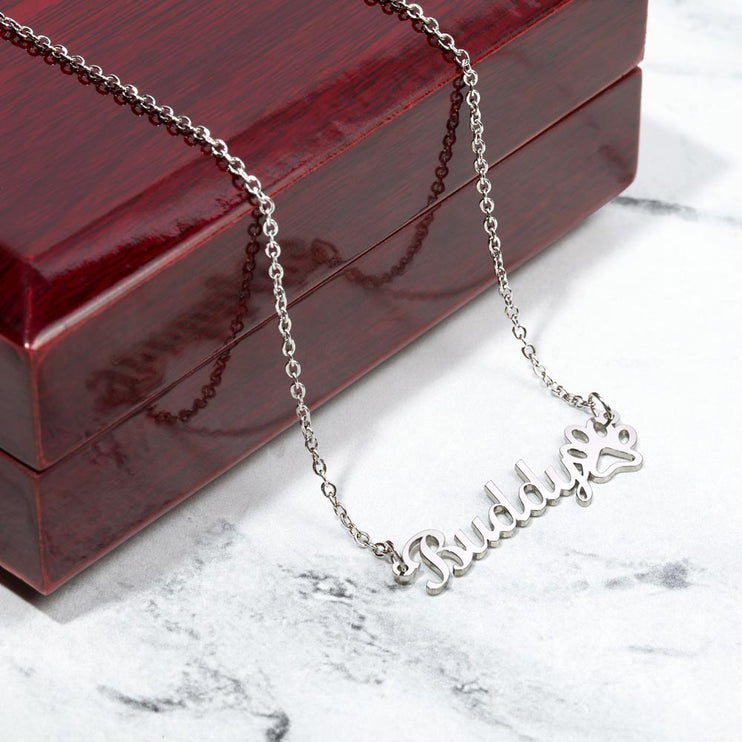 A polished stainless-steel pet name paw print necklace on top of mahogany box.