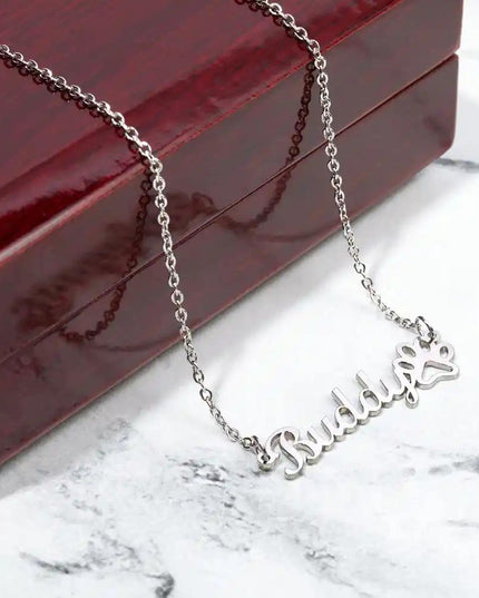 Pet Name Paw Print Necklace with a polished stainless-steel variant hanging off of the top of a mahogany box on a white marble table