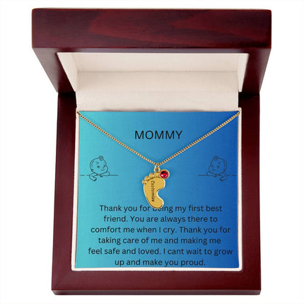 a yellow gold baby feet birthstone necklace in a mahogany box