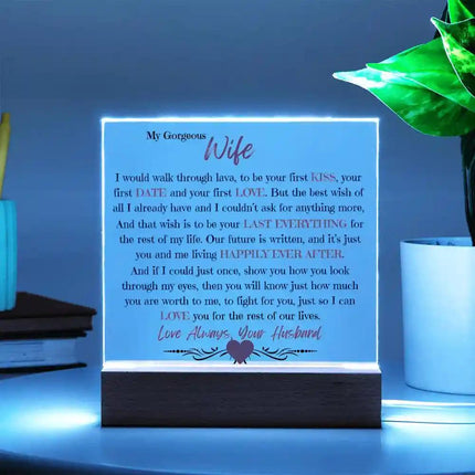 Acrylic Square Plaque with wood base on a white table with the blue LED light on and with a potted plant to the right of it.