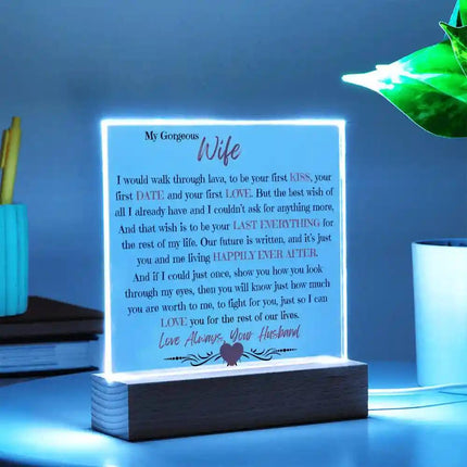Acrylic Square Plaque with wood base on a white table with the blue LED light on and with a potted plant to the right of it slightly angled to the right. 