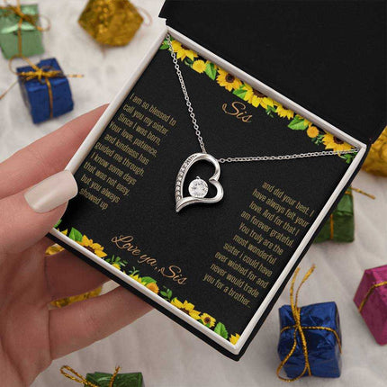 Forever Love Necklace with a white gold charm on a To Sis from Sis greeting card up close in a models hand in a two-tone box angled slightly to the right