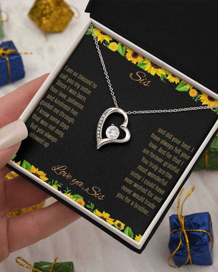 Forever Love Necklace with a white gold charm on a To Sis from Sis greeting card up close in a models hand in a two-tone box angled slightly to the right
