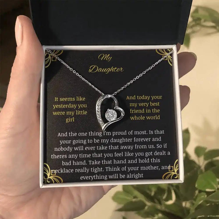 Forever Love Necklace with a white gold charm in a two-tone box with a greeting card to daughter from mom held in a hand further away