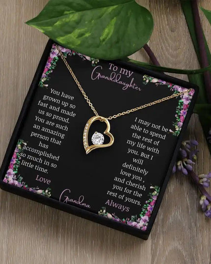 Forever Love Necklace with a yellow gold charm on a for granddaughter from grandpa greeting card in a two-tone box on a table angled left with a green plant beside it