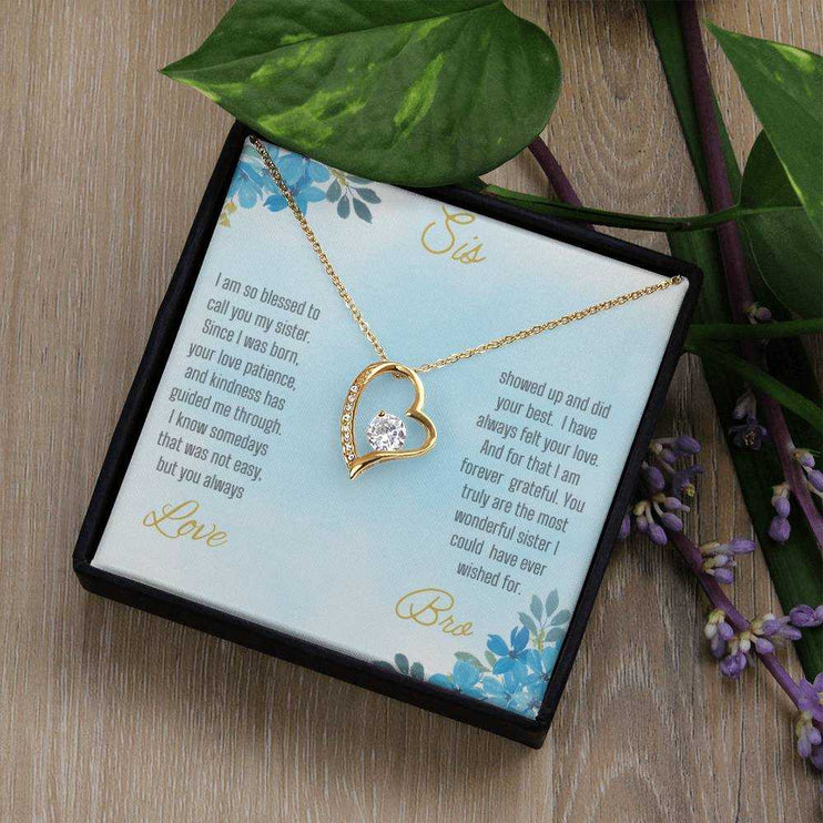 Forever Love Necklace with a yellow gold variant on a to sis from bro greeting card close up view in a two-tone box angled slightly to the right on a light tan table.